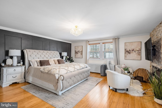 bedroom featuring crown molding, a notable chandelier, a stone fireplace, and light hardwood / wood-style flooring