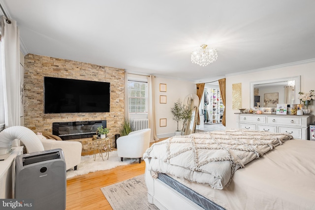 bedroom featuring a stone fireplace, radiator, ornamental molding, an inviting chandelier, and light hardwood / wood-style flooring