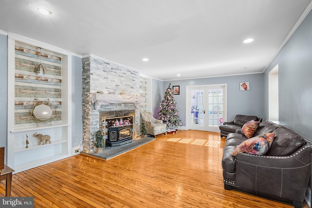 living room with built in features, a wood stove, hardwood / wood-style flooring, ornamental molding, and french doors