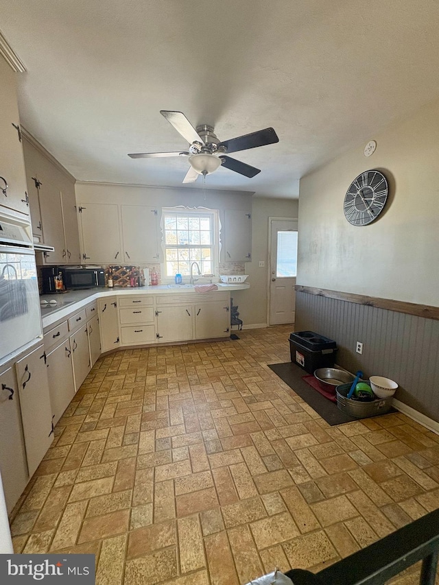 kitchen featuring ceiling fan, oven, sink, and white cabinets