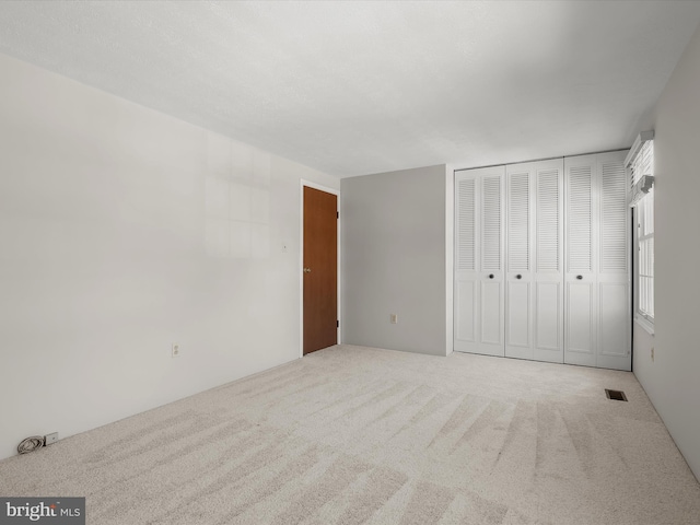 unfurnished bedroom with light colored carpet and a closet