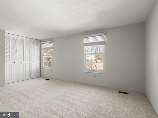 unfurnished bedroom with multiple windows, light carpet, and a closet