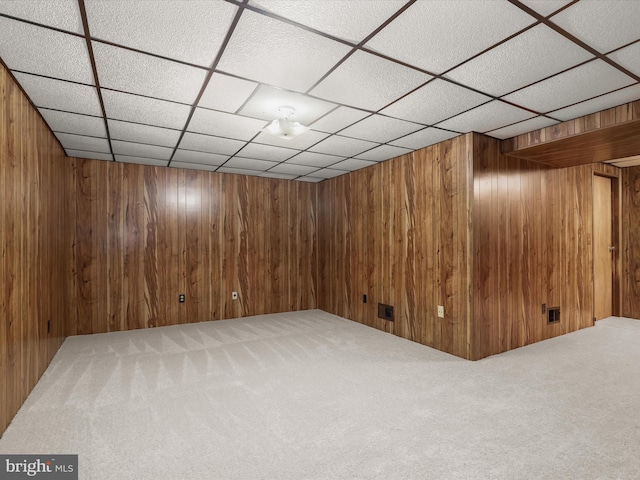 basement featuring a drop ceiling, carpet floors, and wooden walls