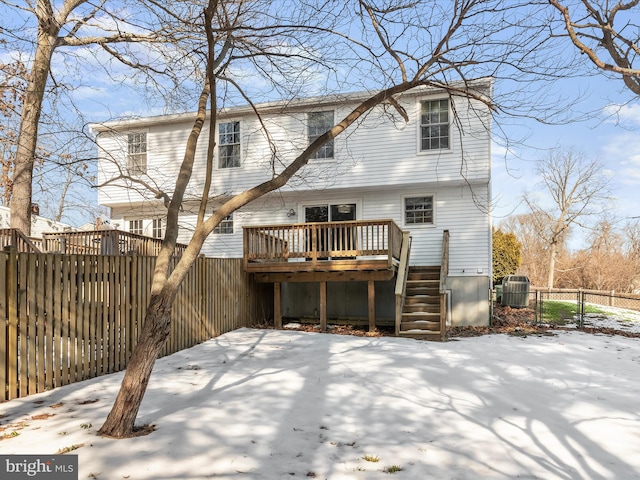 snow covered back of property with cooling unit and a wooden deck