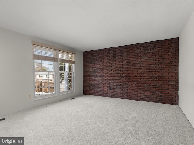 carpeted empty room featuring brick wall