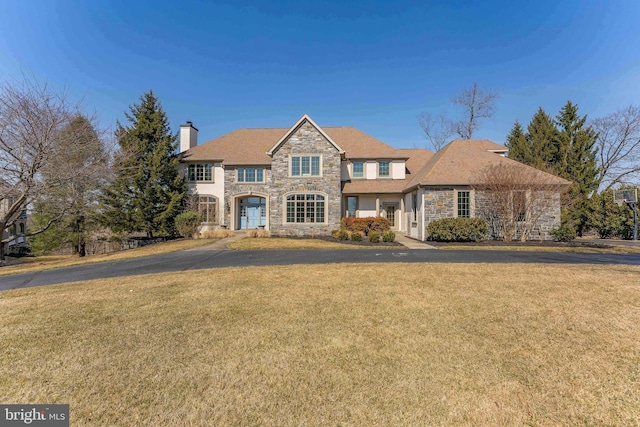 traditional-style home featuring stone siding, a chimney, and a front lawn