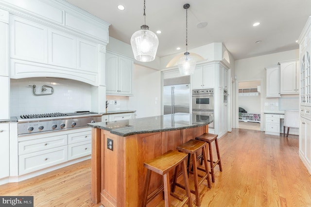 kitchen with a center island, a breakfast bar area, light wood-style flooring, appliances with stainless steel finishes, and white cabinetry