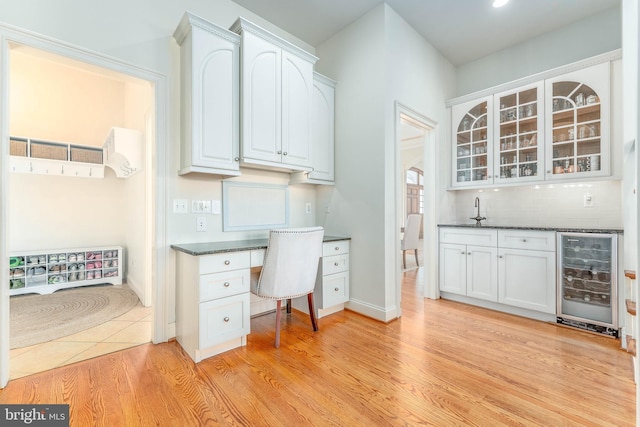 unfurnished office featuring wine cooler, built in desk, bar, light wood-style floors, and a sink