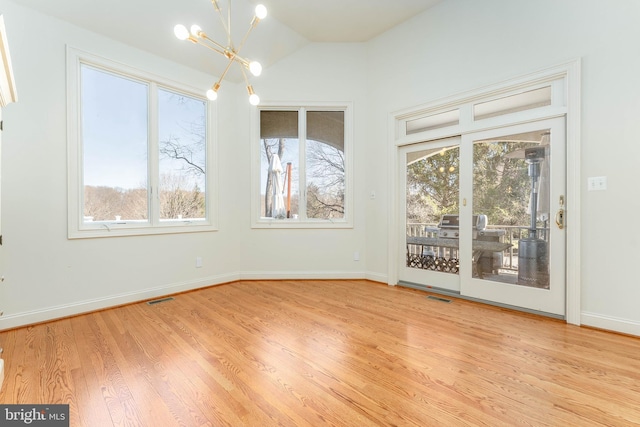 empty room with an inviting chandelier, wood finished floors, visible vents, and baseboards