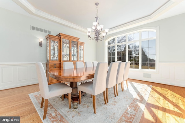 dining area featuring visible vents, a wainscoted wall, light wood-style flooring, a tray ceiling, and an inviting chandelier