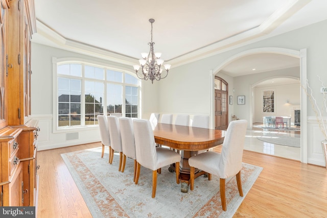 dining room with a tray ceiling, ornamental molding, an inviting chandelier, light wood-style floors, and arched walkways