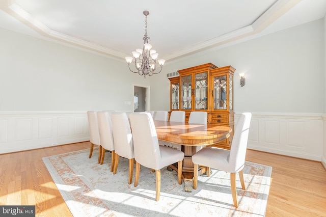 dining room with an inviting chandelier, light wood-style flooring, crown molding, and wainscoting