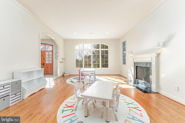 living area with a high end fireplace, baseboards, light wood-style flooring, and crown molding