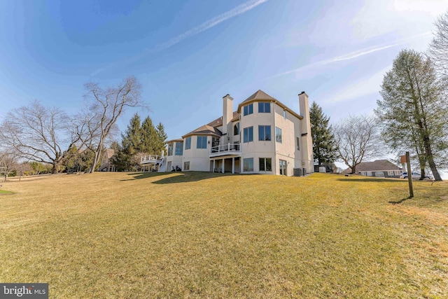 back of property with central AC unit, stucco siding, a chimney, a balcony, and a yard