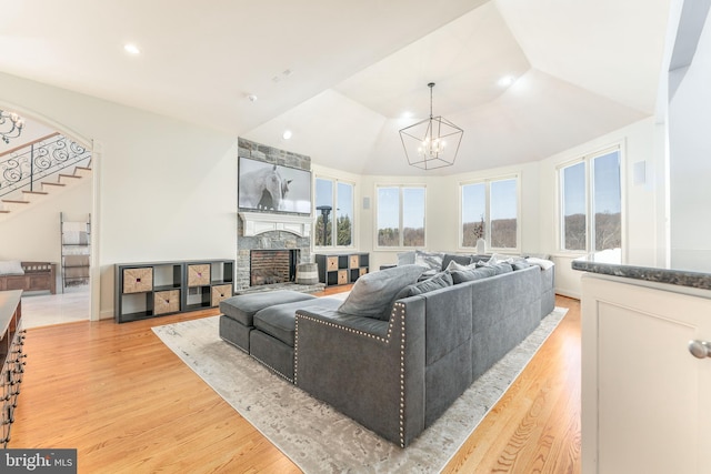 living room featuring stairs, vaulted ceiling, light wood-style flooring, a fireplace, and an inviting chandelier