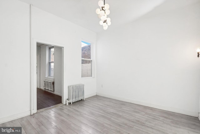 spare room featuring radiator, an inviting chandelier, and light wood-type flooring