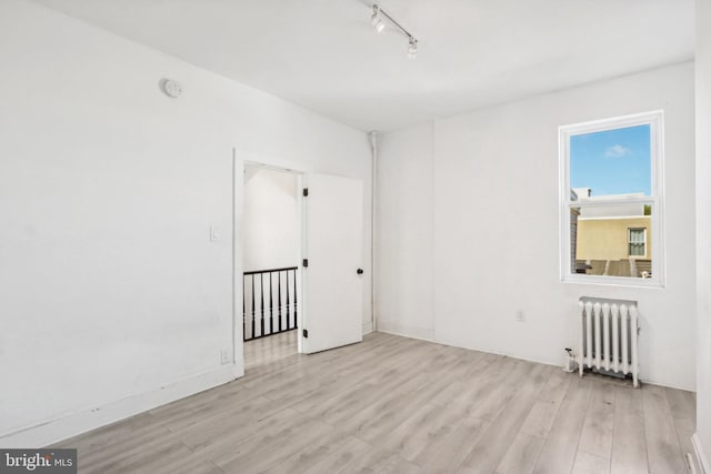 unfurnished room with radiator heating unit, rail lighting, and light wood-type flooring