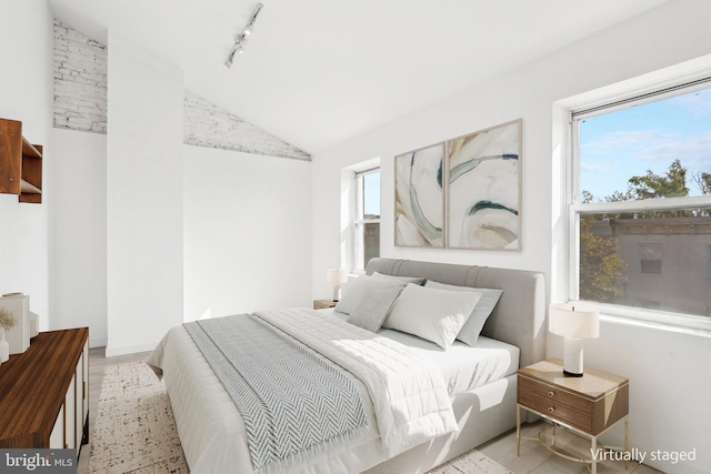 bedroom with track lighting, lofted ceiling, and light wood-type flooring