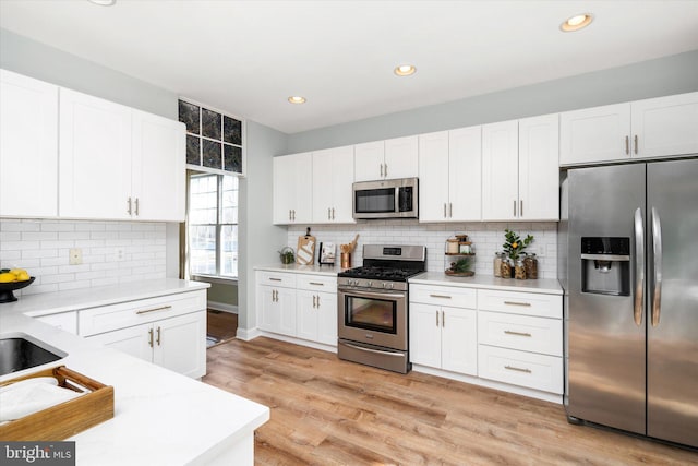 kitchen with stainless steel appliances, tasteful backsplash, white cabinets, and light hardwood / wood-style floors