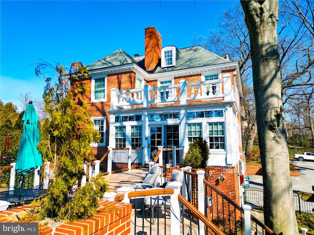 back of property with brick siding, a chimney, fence, and a balcony