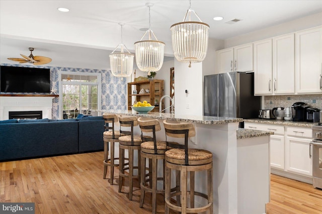 kitchen featuring appliances with stainless steel finishes, pendant lighting, white cabinetry, a kitchen island with sink, and light stone counters