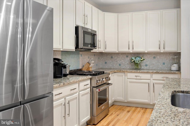 kitchen featuring light stone counters, tasteful backsplash, white cabinets, and appliances with stainless steel finishes