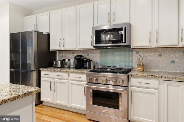 kitchen featuring light stone counters, tasteful backsplash, light hardwood / wood-style flooring, stainless steel appliances, and white cabinets