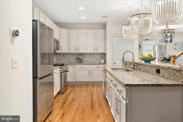 kitchen with pendant lighting, appliances with stainless steel finishes, sink, and white cabinets