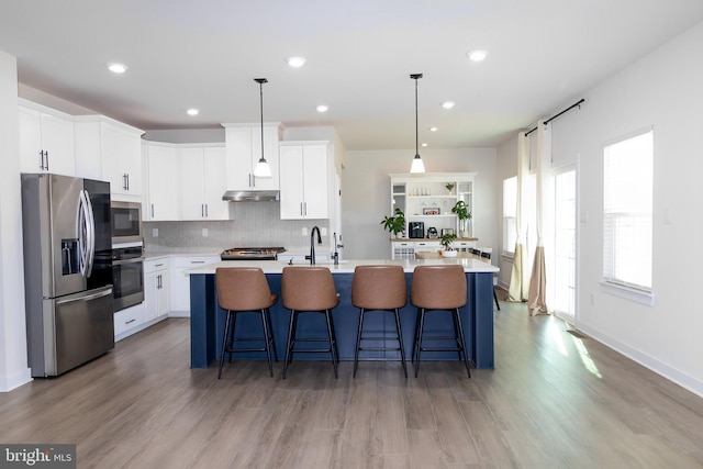 kitchen featuring an island with sink, white cabinetry, stainless steel appliances, and decorative light fixtures