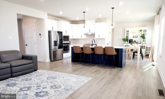 kitchen featuring white cabinets, hanging light fixtures, appliances with stainless steel finishes, and a kitchen island with sink