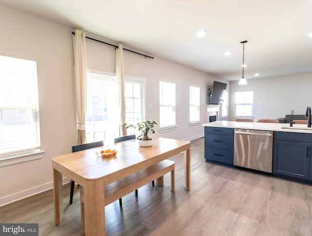 kitchen with sink, blue cabinets, light hardwood / wood-style floors, stainless steel dishwasher, and hanging light fixtures