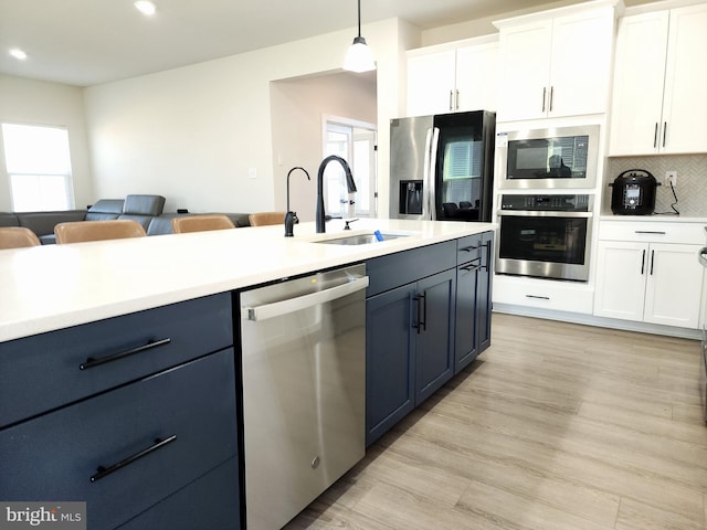 kitchen with sink, blue cabinetry, stainless steel appliances, white cabinets, and hanging light fixtures