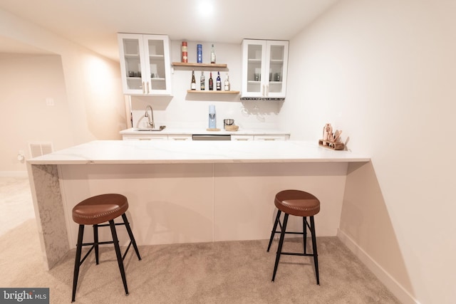 bar featuring stainless steel dishwasher, sink, light carpet, and white cabinets