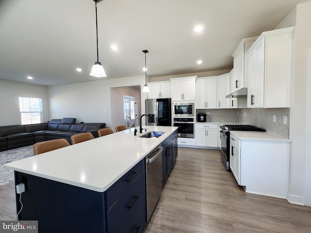 kitchen with an island with sink, appliances with stainless steel finishes, white cabinets, and pendant lighting