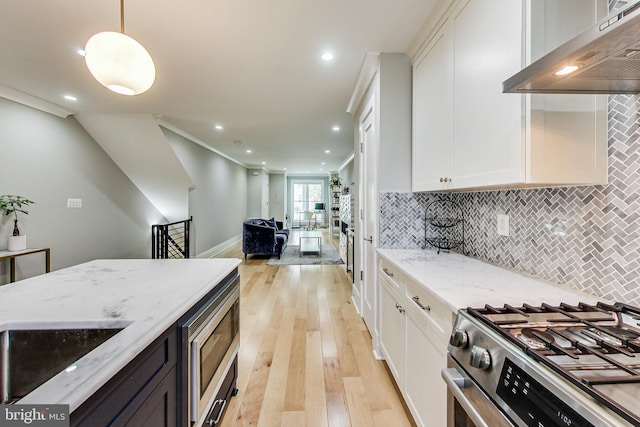 kitchen with decorative light fixtures, white cabinetry, stainless steel appliances, light stone countertops, and wall chimney range hood