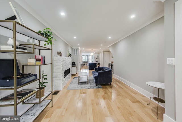 living room featuring crown molding, a stone fireplace, and light hardwood / wood-style flooring