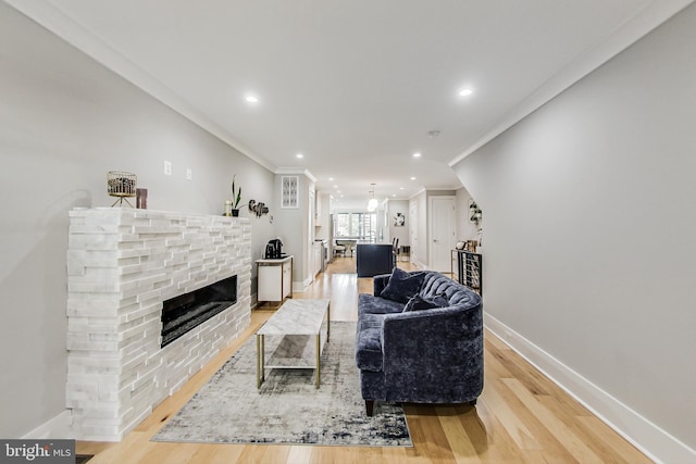 living room with ornamental molding, a stone fireplace, and light hardwood / wood-style flooring