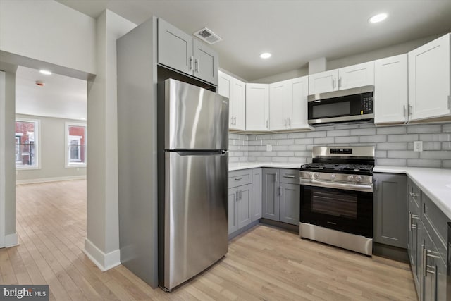 kitchen with white cabinets, appliances with stainless steel finishes, gray cabinetry, and backsplash