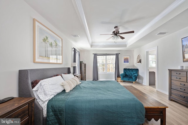 bedroom with ceiling fan, light wood-type flooring, and a tray ceiling