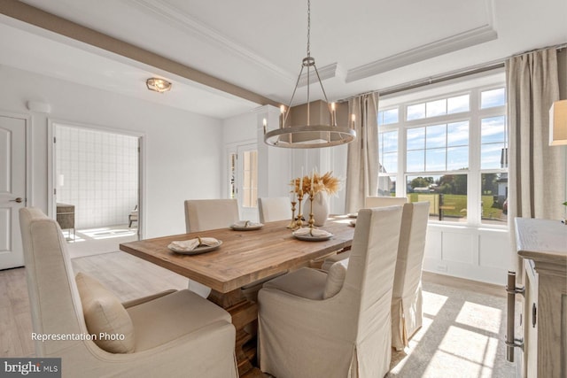 dining space with crown molding, light hardwood / wood-style flooring, a raised ceiling, and a chandelier