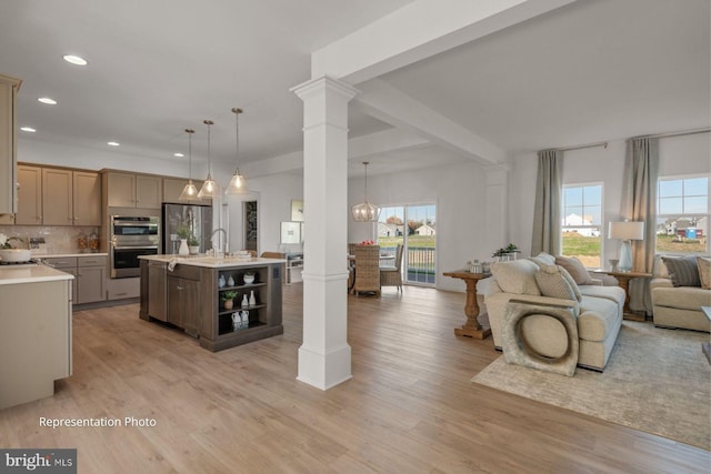 kitchen featuring hanging light fixtures, an island with sink, appliances with stainless steel finishes, and ornate columns