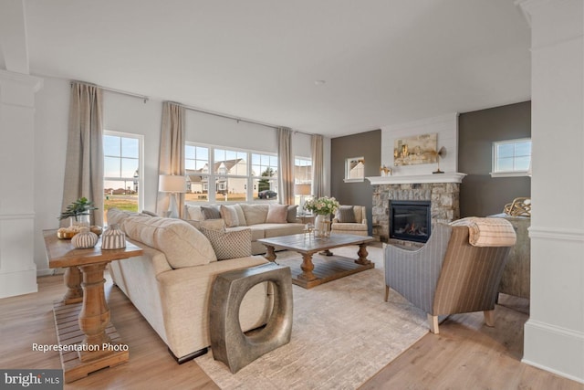 living room featuring a stone fireplace, light hardwood / wood-style flooring, and ornate columns