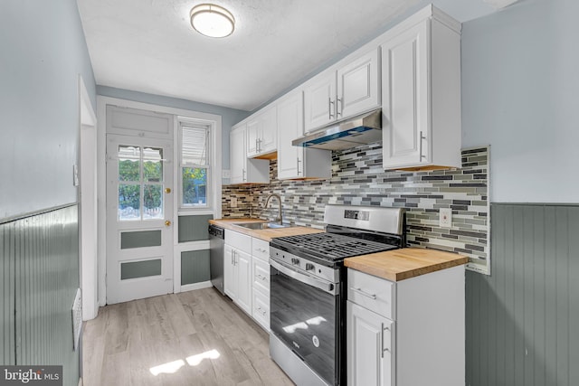 kitchen with under cabinet range hood, a sink, stainless steel appliances, white cabinets, and wooden counters