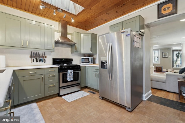 kitchen featuring wall chimney exhaust hood, green cabinetry, a skylight, appliances with stainless steel finishes, and backsplash