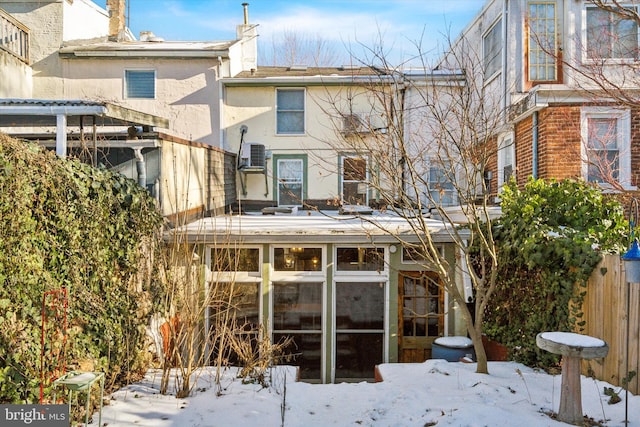 snow covered rear of property featuring a sunroom