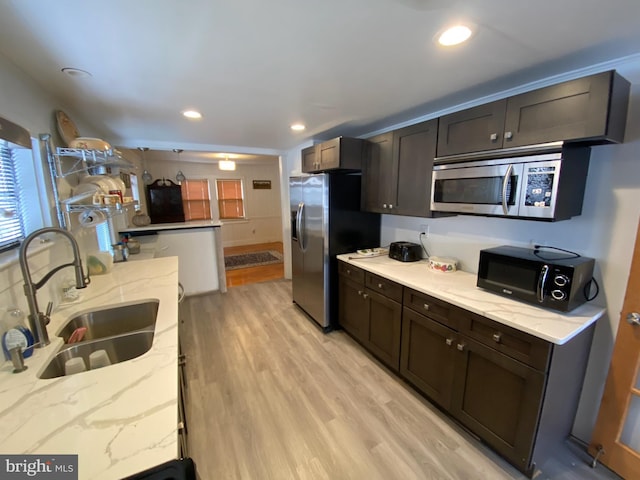 kitchen with sink, light hardwood / wood-style flooring, appliances with stainless steel finishes, dark brown cabinets, and light stone counters