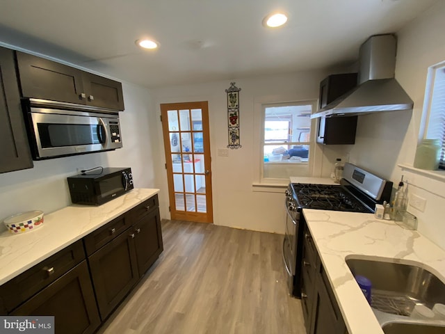 kitchen with sink, dark brown cabinets, stainless steel appliances, wall chimney exhaust hood, and light wood-type flooring