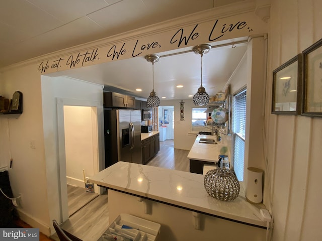 kitchen featuring sink, light hardwood / wood-style flooring, stainless steel appliances, light stone countertops, and decorative light fixtures