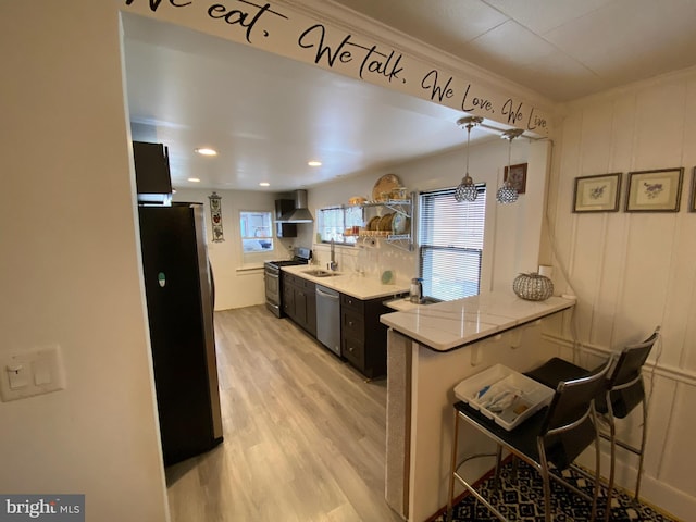 kitchen featuring sink, stainless steel appliances, a kitchen bar, kitchen peninsula, and wall chimney exhaust hood