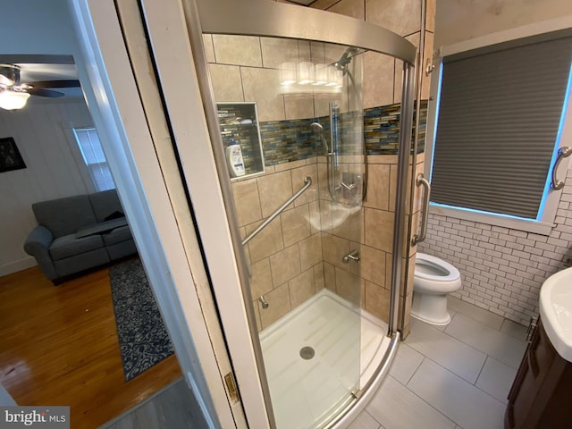 bathroom featuring a shower with shower door, tile walls, tile patterned flooring, ceiling fan, and toilet